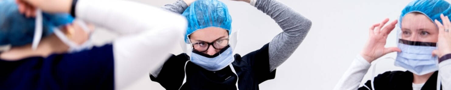 Three students putting on PPE in a classroom